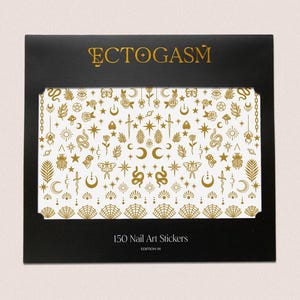 K&ouml;nnte beinhalten: Schwarze Schachtel mit goldenem Text &bdquo;ECTOGASM&ldquo; und einem wei&szlig;en Hintergrund mit goldenen Nagelkunst-Aufklebern mit himmlischem und mystischem Thema. Auf der Schachtel steht &bdquo;150 Nail Art Stickers&ldquo; und &bdquo;Edition III&ldquo;.
