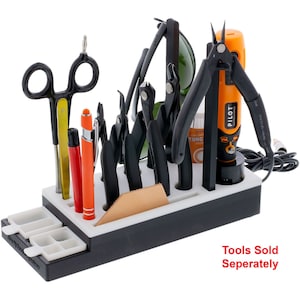 May include: A black and white tool organizer with a variety of tools, including pliers, tweezers, and a small electric screwdriver. The organizer has a white base and a black top. The tools are arranged in slots and there is a small leather pad in the center. The text "Tools Sold Seperately" is printed in red at the bottom of the image.