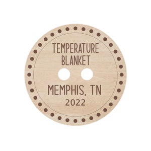 May include: A round wooden button with a brown border and the text "TEMPERATURE BLANKET MEMPHIS, TN 2022" in brown lettering.