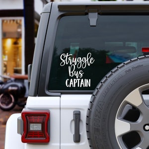 May include: White vinyl sticker on the back window of a gray car. The sticker says "Struggle Bus Captain".