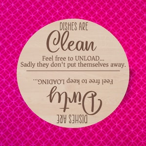 May include: A round wooden sign with a pink and white patterned background. The sign says "DISHES ARE Clean Feel free to UNLOAD... Sadly they don't put themselves away. Feel free to keep LOADING... Dirty DISHES ARE"