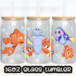 Puede incluir: Tres vasos de vidrio transparente con tapas de bambú y pajitas. Cada vaso presenta un diseño de pez de dibujos animados diferente, incluyendo peces payaso naranjas y peces cirujano azules. El texto "16oz Glass Tumbler" está impreso en la parte inferior.