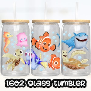 Puede incluir: Tres vasos de vidrio transparente con tapas de madera y pajitas, cada uno con criaturas marinas de dibujos animados. Los diseños incluyen un caballito de mar, un pulpo, una tortuga, un pez payaso y un tiburón. El texto "16oz Glass Tumbler" está en la parte inferior.