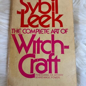 May include: Vintage paperback book titled "Sybil Leek: The Complete Art of Witchcraft." The cover features bold red and pink lettering on a tan background. The book promises to reveal the mystery behind magic powers.