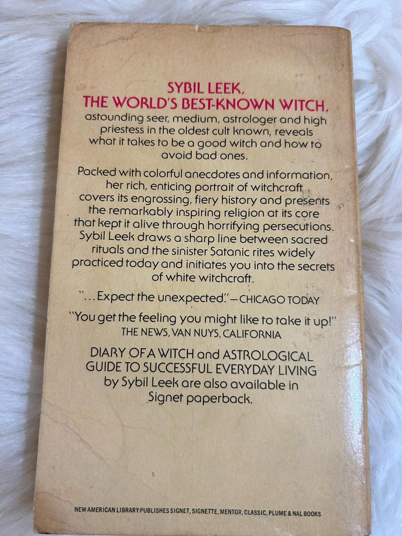 May include: The back cover of a vintage paperback book titled "The World's Best-Known Witch" by Sybil Leek. The cover is tan with black text, including quotes and a brief description of the book's contents.