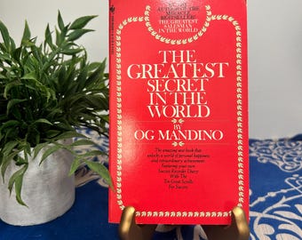 May include: A red book titled "The Greatest Secret in the World" by Og Mandino. The book cover features a gold border with a repeating pattern.