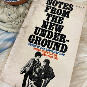 May include: Vintage paperback book titled "Notes From The New Underground" with black text on a cream-colored cover. The cover features a black and white image of three people and the author's name, Jesse Kornbluth.