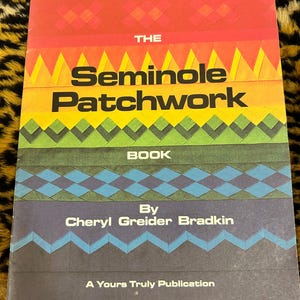 Puede incluir: El libro "Seminole Patchwork" de Cheryl Greider Bradkin, una publicación de Yours Truly. La portada presenta un patrón geométrico colorido en rojo, naranja, amarillo, verde, azul y negro.