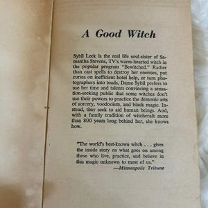 May include: Open book pages with the title "A Good Witch" in a serif font. The text describes Sybil Leek, a real-life witch, and her approach to witchcraft. The book's pages are aged with a cream color.
