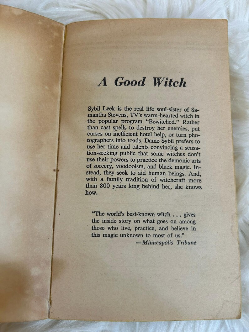 May include: Open book pages with the title "A Good Witch" in a serif font. The text describes Sybil Leek, a real-life witch, and her approach to witchcraft. The book's pages are aged with a cream color.