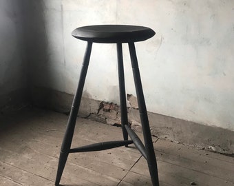 May include: A black wooden stool with a round seat and three legs. The stool is standing on a wooden floor.