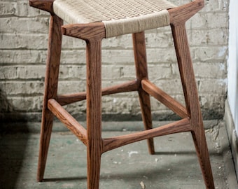 May include: A wooden stool with a woven seat. The stool has a dark brown stain and a simple, modern design.