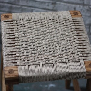 May include: A wooden stool with a woven seat made of natural fiber rope. The seat is woven in a tight, intricate pattern.