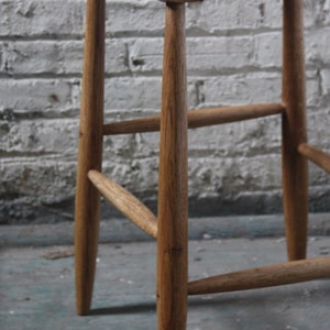 May include: A wooden stool with a woven seat. The stool has four legs and a simple design.
