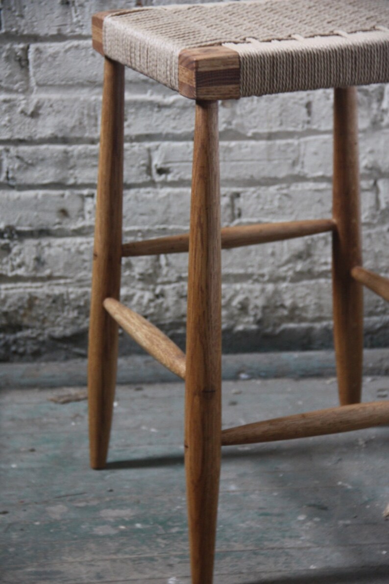 May include: A wooden stool with a woven seat. The stool has four legs and a simple design.