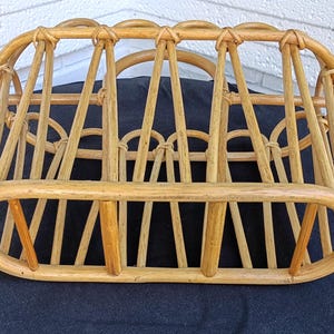 Puede incluir: Un revistero de rat&aacute;n tejido de color marr&oacute;n claro. El revistero tiene una forma rectangular redondeada con soportes verticales y detalles superiores arqueados. Los tonos de madera natural y el dise&ntilde;o abierto crean una soluci&oacute;n de almacenamiento r&uacute;stica. Para revistas.
