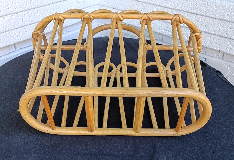 Puede incluir: Un revistero de rat&aacute;n tejido de color marr&oacute;n claro. El revistero tiene una forma rectangular redondeada con soportes verticales y detalles superiores arqueados. Los tonos de madera natural y el dise&ntilde;o abierto crean una soluci&oacute;n de almacenamiento r&uacute;stica. Para revistas.