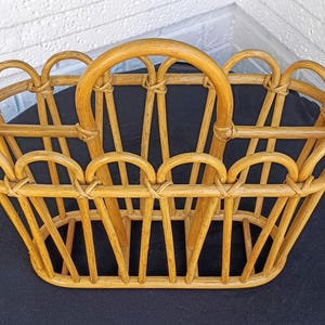 Puede incluir: Una cesta de rat&aacute;n tejido de color marr&oacute;n claro con un asa. La cesta tiene una base rectangular y una serie de aberturas arqueadas a los lados. El asa es una pieza grande y curvada de rat&aacute;n. La cesta est&aacute; dise&ntilde;ada para transportar objetos.