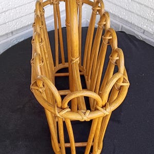Puede incluir: Una cesta de rat&aacute;n tejido de color marr&oacute;n claro, con un dise&ntilde;o alto y abierto. La cesta presenta soportes verticales y asas arqueadas, creando un elemento de almacenamiento decorativo y funcional. Adecuada para diversos usos.