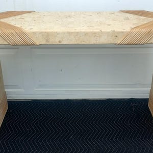 May include: A beige console table with a curved design. The table features a speckled surface and is accented with woven rattan detailing at the corners and base. The table is approximately 48 inches long, 16 inches wide, and 30 inches high.