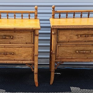 May include: A pair of light brown wooden nightstands featuring a faux bamboo design. Each nightstand has two drawers with horizontal handles and a decorative spindle gallery rail along the top edge. The legs are shaped to resemble bamboo stalks.