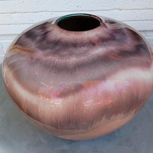 May include: A large, round ceramic vase with a wide opening. The vase has a glossy finish with a color gradient from light pink to deep purple. The interior is dark, and the rim has a teal accent. The vase is a decorative home decor item.