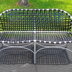 May include: A set of outdoor furniture consisting of a two-person bench and two matching side tables. The bench and tables feature silver-toned metal frames and black woven strap seating and tabletops with a textured glass surface.