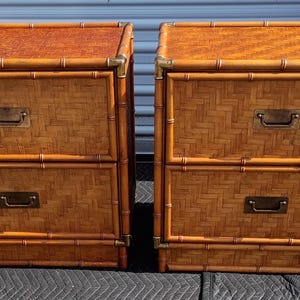 May include: A pair of two-drawer nightstands constructed with a bamboo-style frame and woven rattan panels. Each unit features brass corner accents and rectangular brass drawer pulls. The top surfaces display a textured, patterned finish.