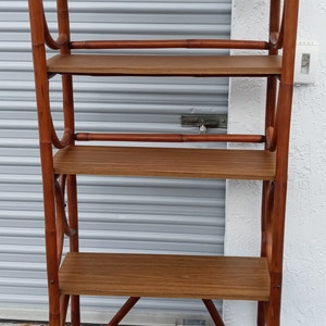 May include: A brown wooden shelf unit with five shelves. The shelves are made of wood and the frame is made of bamboo. The shelf unit is standing on a blue rug.