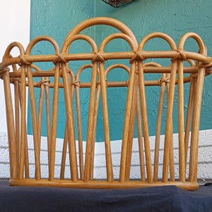 Puede incluir: Un revistero de rat&aacute;n marr&oacute;n claro con asa. El revistero tiene forma rectangular con listones verticales y detalles arqueados en la parte superior. Los tonos de madera natural y el dise&ntilde;o tejido le dan una est&eacute;tica r&uacute;stica y vintage.