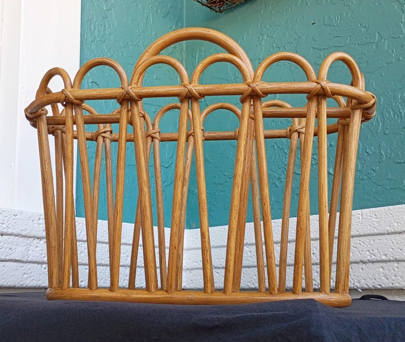 Puede incluir: Un revistero de rat&aacute;n marr&oacute;n claro con asa. El revistero tiene forma rectangular con listones verticales y detalles arqueados en la parte superior. Los tonos de madera natural y el dise&ntilde;o tejido le dan una est&eacute;tica r&uacute;stica y vintage.