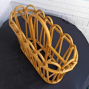 Puede incluir: Un revistero de rat&aacute;n marr&oacute;n claro. El revistero tiene forma rectangular con asa y detalles decorativos arqueados. El dise&ntilde;o tejido es visible en toda la pieza, mostrando su artesan&iacute;a.