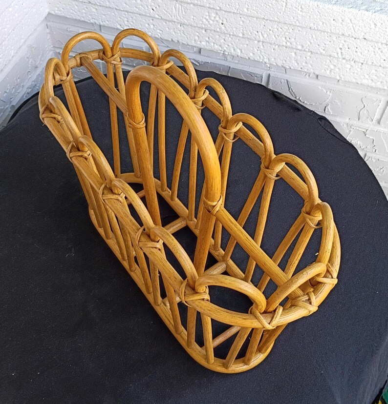 Puede incluir: Un revistero de rat&aacute;n marr&oacute;n claro. El revistero tiene forma rectangular con asa y detalles decorativos arqueados. El dise&ntilde;o tejido es visible en toda la pieza, mostrando su artesan&iacute;a.