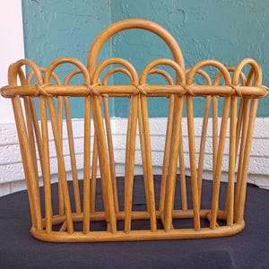 Puede incluir: Un revistero de rat&aacute;n marr&oacute;n claro con un asa curva. El revistero tiene forma rectangular con listones verticales y detalles arqueados a lo largo del borde superior. Los tonos de madera natural crean una est&eacute;tica c&aacute;lida y acogedora.