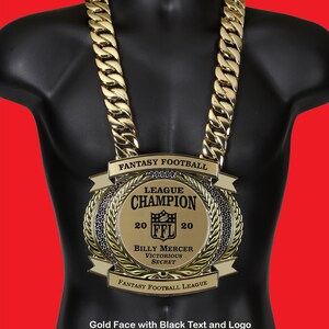 May include: A gold chain necklace with a large gold pendant. The pendant is a fantasy football league championship trophy with black text and a black logo. The text on the pendant reads "Fantasy Football League Champion 20 FFL 20 Billy Mercer Victorious Secret Fantasy Football League".