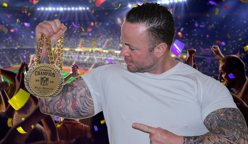 May include: A man wearing a white t-shirt holds aloft a gold chain with a large gold medal. The medal reads "League Champion 2020" and features a football logo. The man is standing in front of a stadium with a crowd of cheering fans.