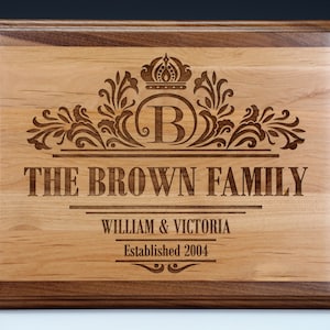 May include: A wooden plaque with a decorative design featuring a crown, floral elements, and the letter "B". The text "The Brown Family, William & Victoria, Established 2004" is engraved on the plaque.