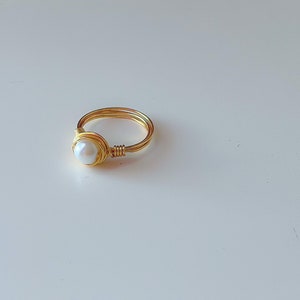 May include: A gold wire ring with a white pearl in the center.