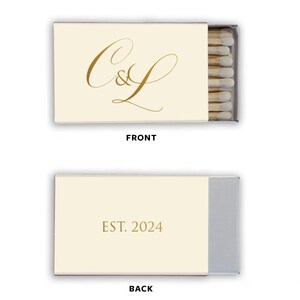 Op de afbeelding: Een wit luciferdoosje met een gouden kalligrafiemonogram "C&L" op de voorkant en "EST. 2024" op de achterkant.
