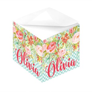 Peut inclure: Un bloc-notes blanc avec un motif floral et un motif vichy. Le bloc-notes porte le nom "Olivia" écrit en rouge.