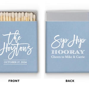 May include: Two light blue matchboxes. The front box has the text "the Hoyton's" and "OCTOBER 27, 2024". The back box says "Sip Hip HOORAY Cheers to Mike & Carrie". The match heads are visible.