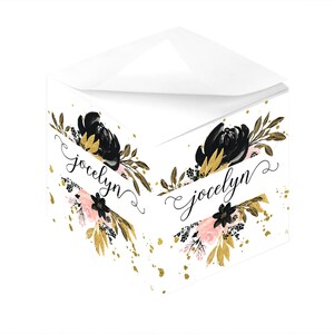 Könnte beinhalten: Ein weißer Notizblock mit einem schwarzen und goldenen Blumendesign und dem Namen "Jocelyn" in Kursivschrift auf einem Banner. Der Notizblock ist mit goldenem Glitzer verziert.
