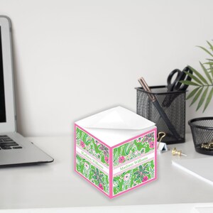 Könnte beinhalten: Ein Notizblock mit grünem und rosafarbenem Blumenmuster, auf dem der Name "Madline Williams" aufgedruckt ist. Der Notizblock steht auf einem weißen Schreibtisch.