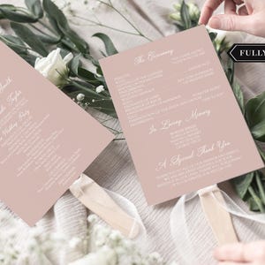 May include: Two blush pink wedding fans with white text. One fan features a monogram and names, the other lists the ceremony details. The fans have wooden handles with white ribbon. The words "FULLY ASSEMBLED" are in a black box.