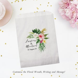 May include: White paper gift bag decorated with a watercolour floral design. The design includes pink, white, and yellow flowers, and green leaves. The bag is personalised with the names "Lauren & Michael" and the date "21 August 19".