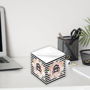 Könnte beinhalten: Ein schwarz-weiß gestreiftes Notizblock mit einem Blumendesign und dem Monogramm "S" in der Mitte. Der Notizblock befindet sich auf einem weißen Schreibtisch mit einem Laptop, einer Pflanze und anderen Büroartikeln.