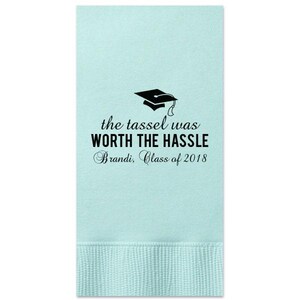 May include: Light blue paper napkins with a black graduation cap and the text "the tassel was WORTH THE HASSLE Brandi, Class of 2018".