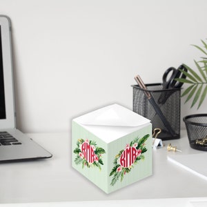 Könnte beinhalten: Ein grüner und weißer Notizblock mit einem Blumendesign und dem Monogramm "KMB" in Rot. Der Notizblock steht auf einem weißen Schreibtisch.