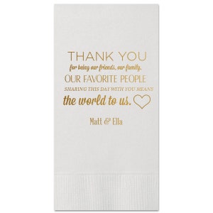 Pode incluir: Guardanapo de papel branco com texto dourado que diz "THANK YOU for being our friends, our family, OUR FAVORITE PEOPLE SHARING THIS DAY WITH YOU MEANS the world to us." com um símbolo de coração dourado. O texto "Matt & Ella" também está em dourado na parte inferior do guardanapo.