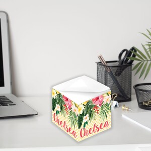 Könnte beinhalten: Ein gelber und weißer karierter Notizblock mit einem tropischen Blumendesign und dem Namen "Chelsea" in rosa. Der Notizblock befindet sich auf einem weißen Schreibtisch mit einem Laptop, einer Pflanze und anderen Büroartikeln.